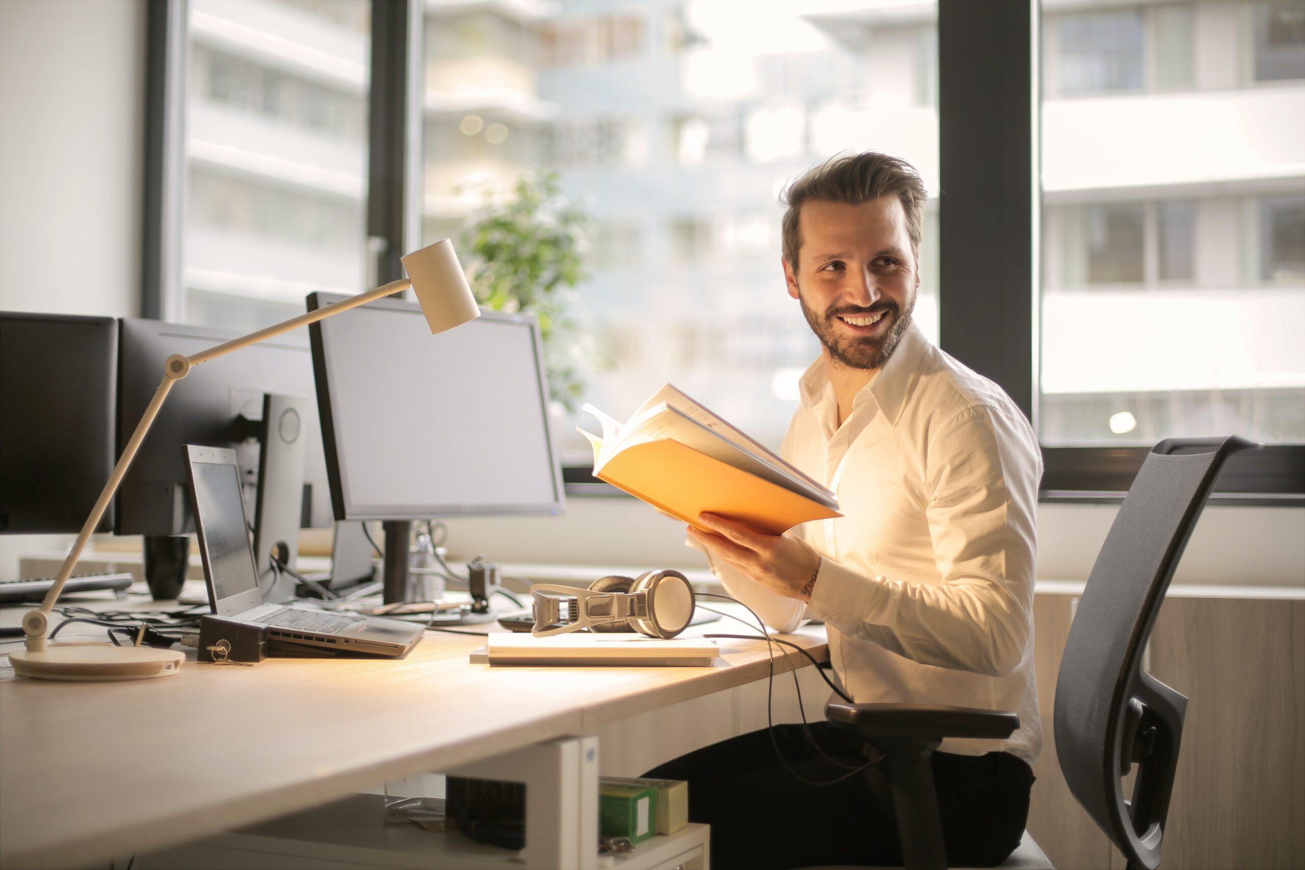 Man som ler och arbetar från en ergonomisk kontorsstol vid ett höj och sänkbart skrivbord